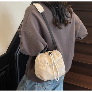 Detail of beige nylon drawstring bucket bag with cat ear logo shown on a model