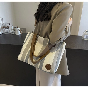 Detail of grey striped canvas tote bag with brown leather straps shown on a model back