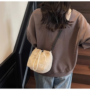 Detailed view of beige drawstring bucket bag featuring a cat logo and adjustable strap