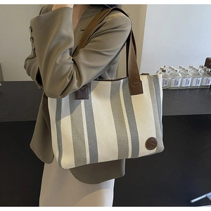 Shoulder shot of a striped canvas tote bag with brown straps and a leather logo patch