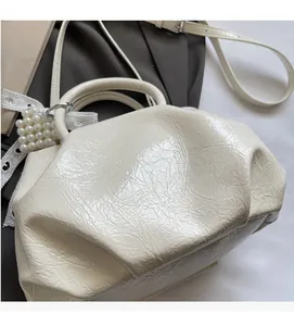 Close-up of pleated cream leather texture and pearl charm detail on a stylish handbag