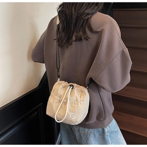 Detail of beige drawstring bucket bag with cat ear embroidery on wooden stairs