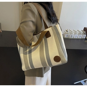 Detailed view of striped canvas tote bag with brown woven straps worn by a model