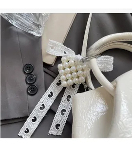 Detail of white pearl heart charm with lace ribbons on a white patent leather bag handle