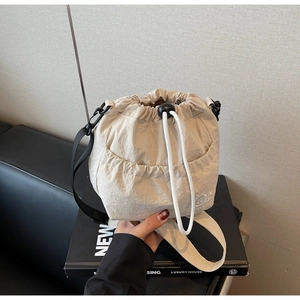 Detail of beige pleated fabric bucket bag showing white drawstring and black strap