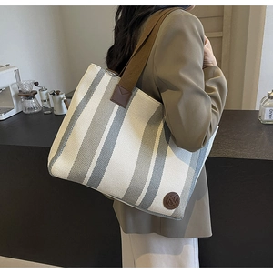 Detailed view of canvas striped tote bag with leather logo patch and brown straps