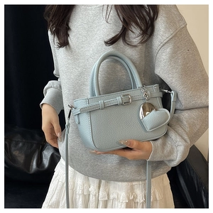 Detail of light blue lychee pattern crossbody bag with heart charm and silver strap buckle