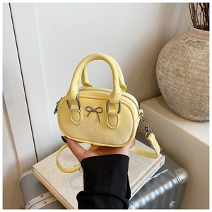 Detailed shot of yellow mini bow handbag held by hand with luggage and books background