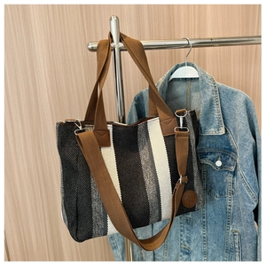 Detail of striped canvas tote bag featuring brown fabric handles and adjustable strap
