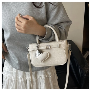 Detail of cream lychee texture handbag with elegant buckle and heart-shaped pendant
