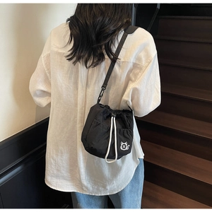 Detail of black drawstring bucket bag with cat graphic worn by model on stairs