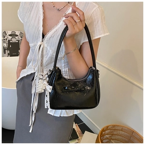 Detail der schwarzen glänzenden Handtasche mit Schleife und Perlenanhänger am Model