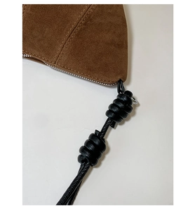 Détail du sac en daim marron avec bandoulière en cuir noué et coutures de précision