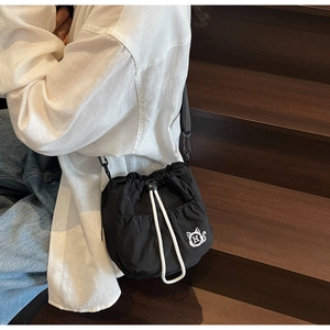 Detail of black drawstring bucket bag with cat embroidery logo on casual outdoor setting