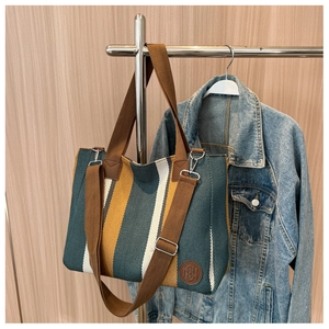 Detail of striped canvas tote with brown straps and embossed logo on wood background