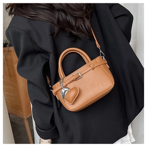 Detail view of brown lychee grain leather crossbody bag with heart pendant on model