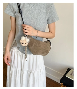 Detail of coffee brown suede croissant bag featuring a beige teddy bear plush charm
