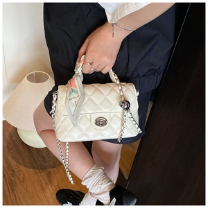 Close-up of beige quilted chain bag featuring a silver twist lock and printed silk scarf