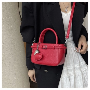 Detail of red litchi texture leather handbag with silver hardware and heart charm decoration