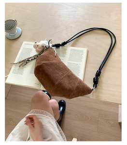 Detail of brown suede croissant bag with knot strap and plush bear charm on wood table