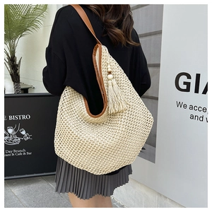 Detail of handwoven straw tote bag with brown leather strap and decorative tassels