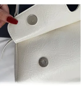 Détail macro de la texture plissée blanc crème et fermoir magnétique en métal du sac