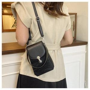 Détail d'un mini sac bandoulière noir avec fermoir métallique ovale sur un mannequin