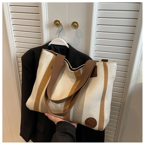 Close-up of off-white canvas tote bag with brown stripes and leather logo detail