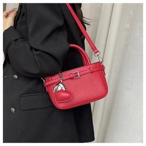 Detail of red litchi grain leather crossbody bag with heart pendant and buckle on model