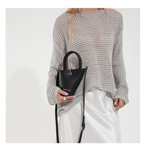 Sac seau chic en cuir litchi noir porté avec un haut en tricot gris et jupe blanche