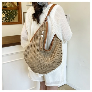 Detail of straw woven tote bag with dark brown leather trim and tassel bead charm