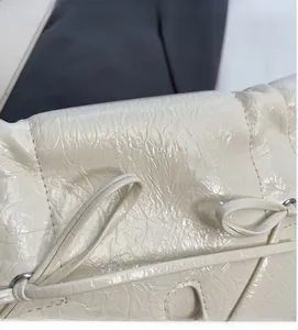 Vue détaillée du cuir verni froissé crème avec nœud élégant et anneaux métalliques
