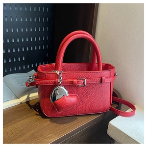 Detail of red lychee pattern handbag with heart charm on a dark wooden surface