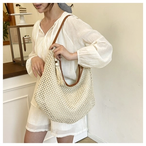 Close-up of beige woven tote bag with brown leather strap and wooden bead tassel detail