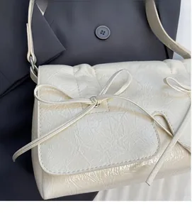 Détail du sac crème en cuir plissé avec nœud décoratif sur fond de veste foncée