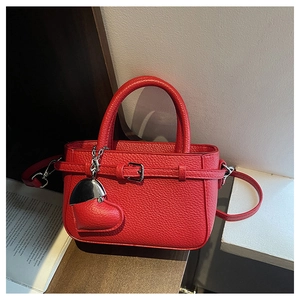 Close-up of red lychee pattern leather bag with heart pendant on dark wooden desk