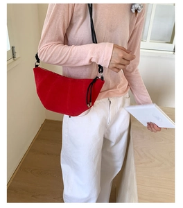Red suede croissant bag worn with black strap over minimalist outfit in natural light