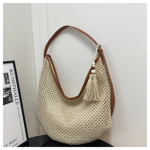 Detail of straw woven crescent tote bag with leather strap and decorative tassel