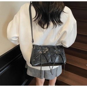 Sac en cuir verni noir brillant avec nœuds porté à l'épaule par un mannequin chic