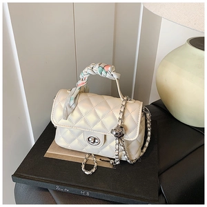 Close-up of quilted ivory handbag with silk scarf handle and silver chain on black stand