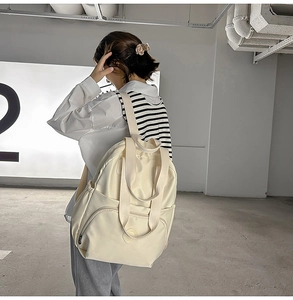 Detailansicht des cremefarbenen Nylon-Rucksacks mit großer Fronttasche und Seitenfächern