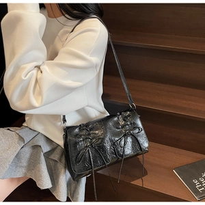 Détail du sac à bandoulière en cuir verni noir brillant avec texture plissée et nœuds