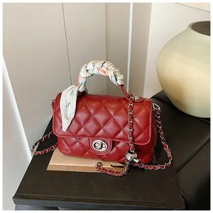 Close-up of red quilted chain bag with silk scarf wrapped handle on decorative books