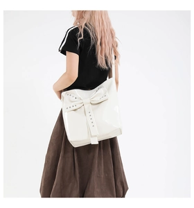 Detail der weißen Handtasche aus Lackleder mit Nieten und großer Schleifenverzierung