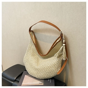 Detail of a straw shoulder bag showing woven texture, brown leather strap and tassel charm