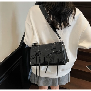 Sac à bandoulière en cuir verni noir avec nœuds doux porté par un mannequin