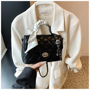 Close-up of quilted black handbag with metal lock and silk scarf wrapped handle detail