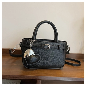 Detail of black lychee leather handbag with heart charm and silver buckle on wood shelf