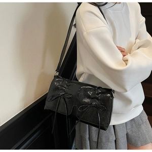 Détail d'un sac à bandoulière noir brillant avec des nœuds élégants et une texture plissée