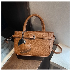 Detail of brown litchi grain leather handbag with heart pendant on a wooden shelf